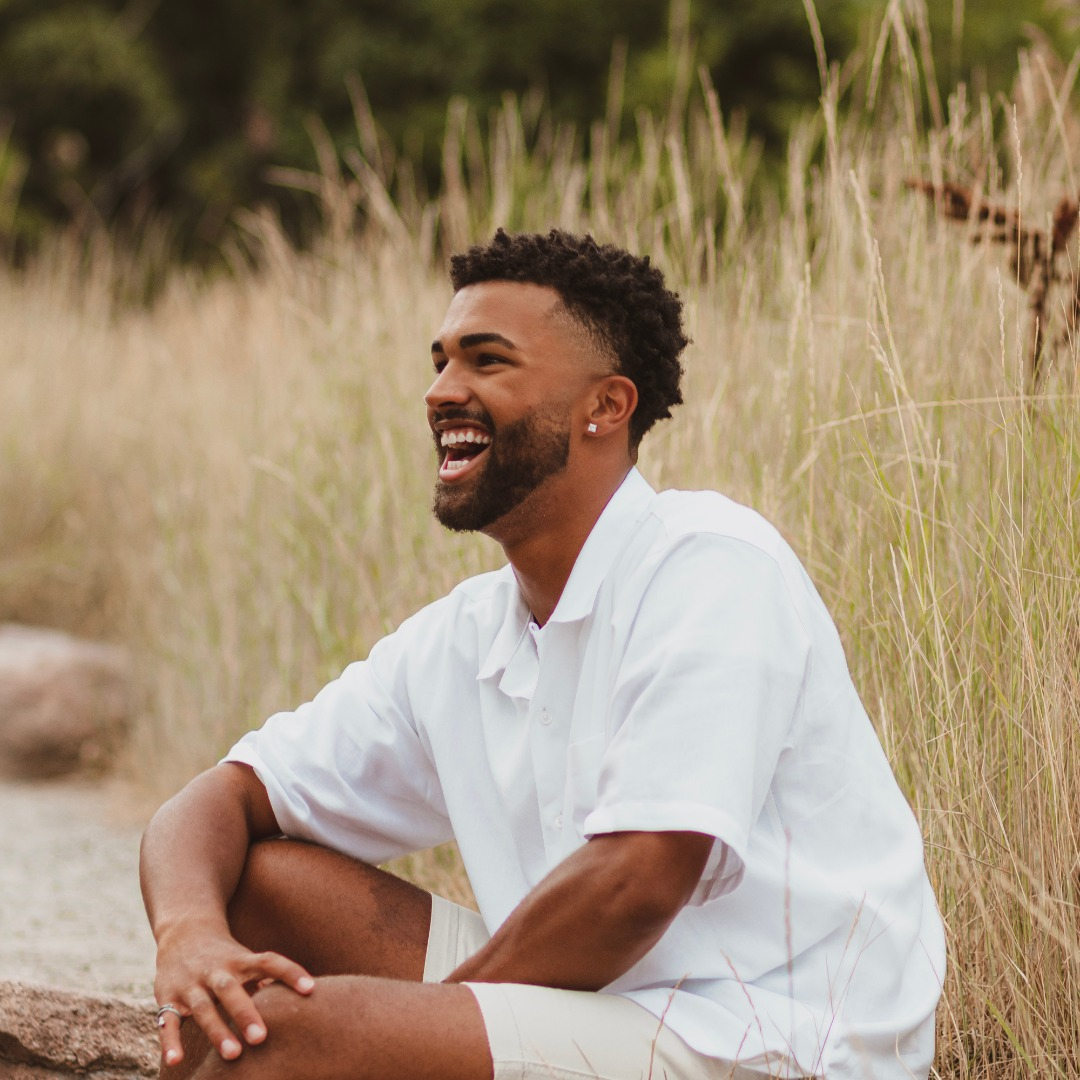 Young, smiling man sitting in tall grass.